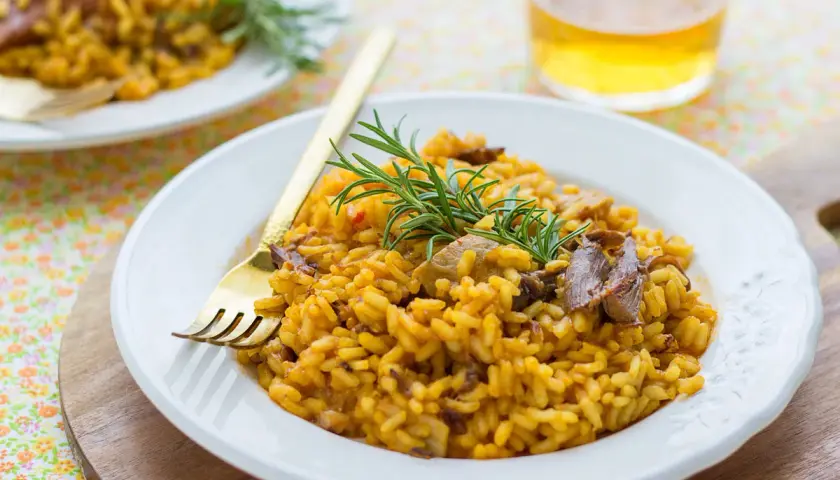 Delicioso arroz con secreto ibérico y setas, adornado con romero fresco. Un plato reconfortante y lleno de sabor.