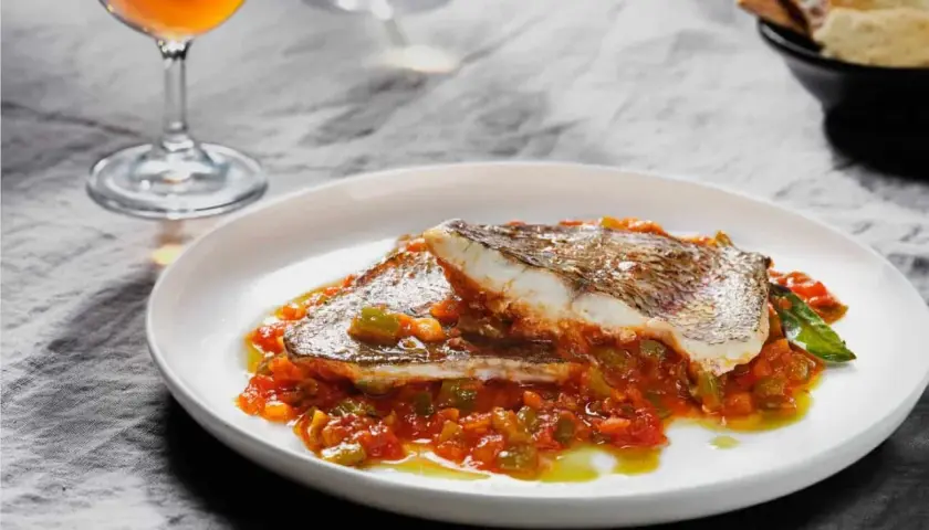 Delicioso plato de urta a la roteña, con pescado blanco y verduras en salsa, acompañado de una copa de vino.