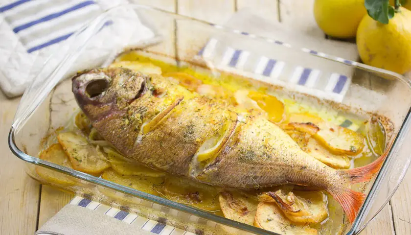 Besugo al horno con patatas y limón, recién sacado del horno en una fuente de cristal.