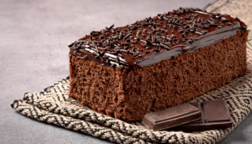 Un delicioso pastel de chocolate cubierto con glaseado y chispas de chocolate, acompañado de trozos de chocolate.