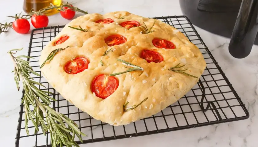 Focaccia receta casera con tomates cherry y romero sobre una rejilla.