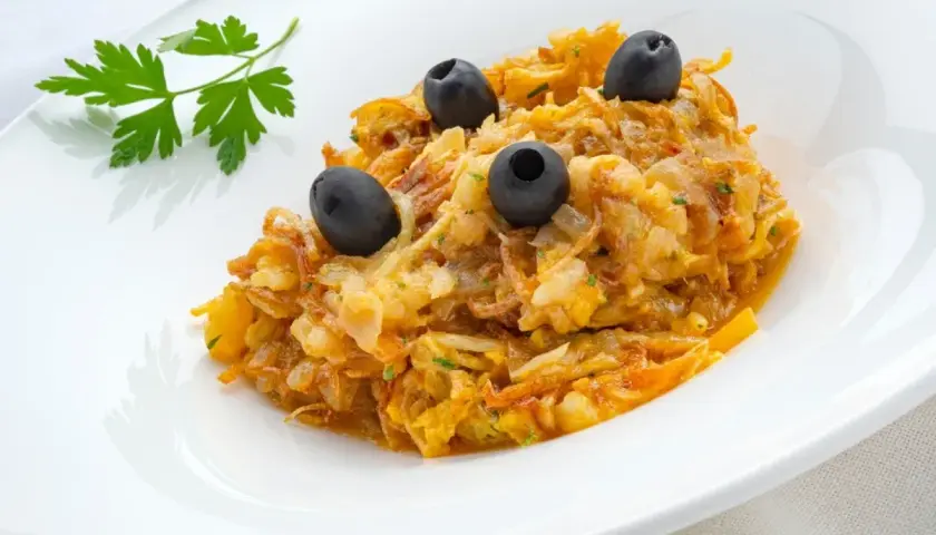 Delicioso revuelto de bacalao con aceitunas negras y perejil fresco, servido en un plato blanco.