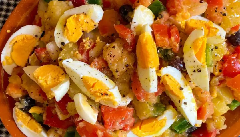 Ensalada campera con patatas, huevos duros, tomate, pimiento y aceitunas negras, todo mezclado y sazonado.