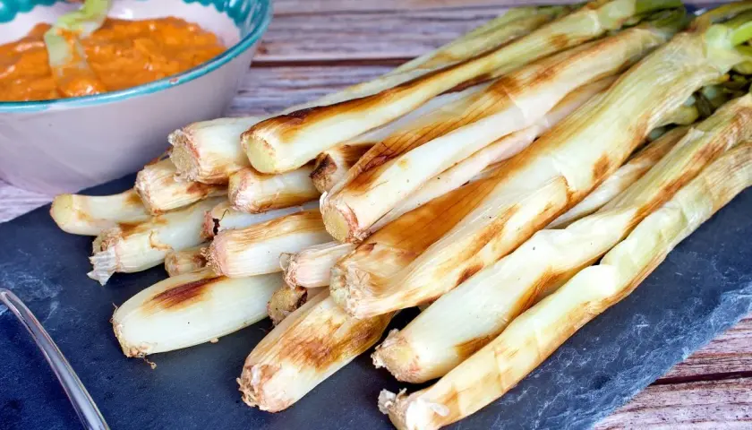 Calçots al horno, tiernos y dorados, listos para mojar en salsa romesco. Un festín de sabor.