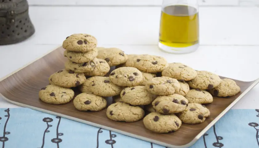 Montón de galletas caseras de pueblo con chispas de chocolate en una bandeja de madera, junto a una botella de aceite de oliva.
