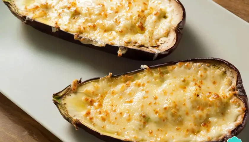 Dos mitades de berenjenas rellenas de carne, gratinadas con queso dorado y burbujeante, listas para disfrutar.