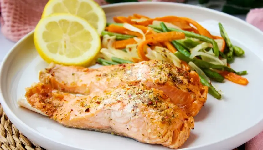 Dos filetes de salmón al microondas con hierbas, acompañados de zanahorias y judías verdes, y rodajas de limón.