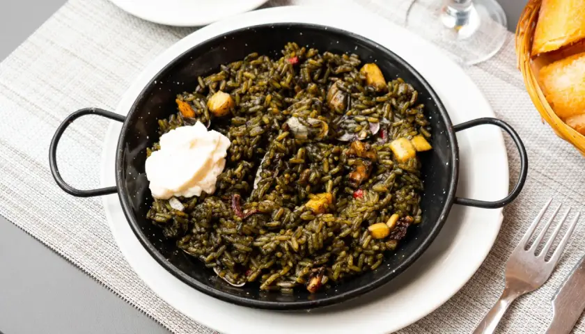 Arroz negro con sepia, servido en paellera con una cucharada de alioli. Se aprecian trozos de sepia y pimientos.