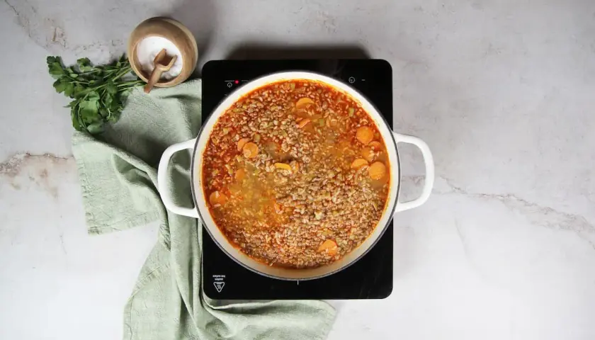 Olla con lentejas con arroz y zanahoria hirviendo. Al lado, perejil fresco y un cuenco de sal.