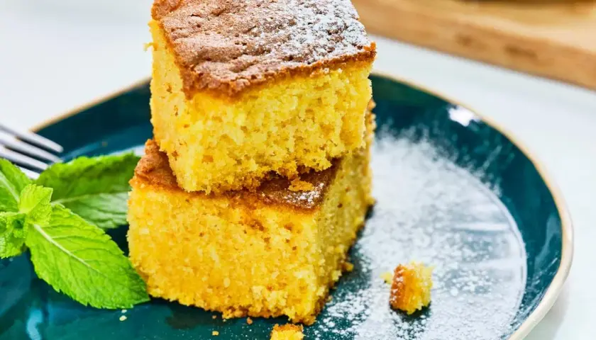 Dos porciones de bizcocho de calabaza apiladas, espolvoreadas con azúcar glas, junto a hojas de menta fresca en un plato azul.