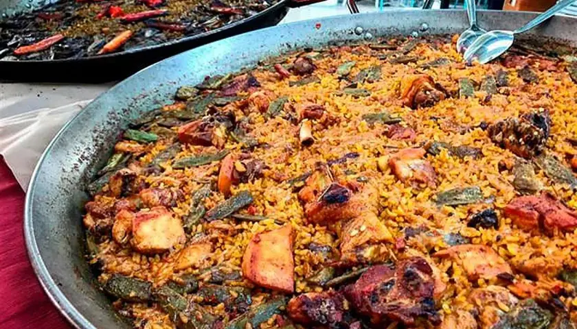 Paella valenciana con pollo, conejo y verduras. Los ingredientes se mezclan con el arroz en esta gran paellera.