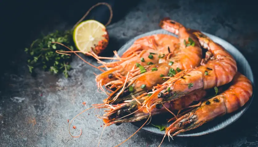 Gambones al horno, jugosos y dorados, servidos con hierbas frescas y rodaja de limón.