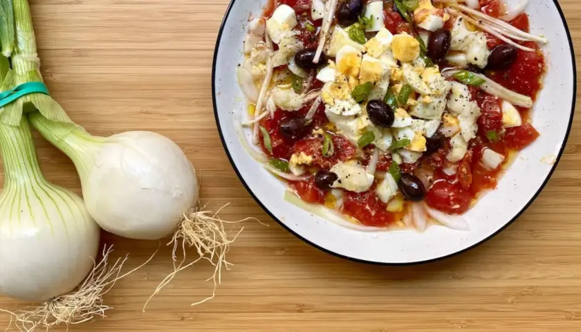Deliciosa ensalada murciana con tomates, huevos duros, aceitunas negras y cebolla tierna, lista para disfrutar.