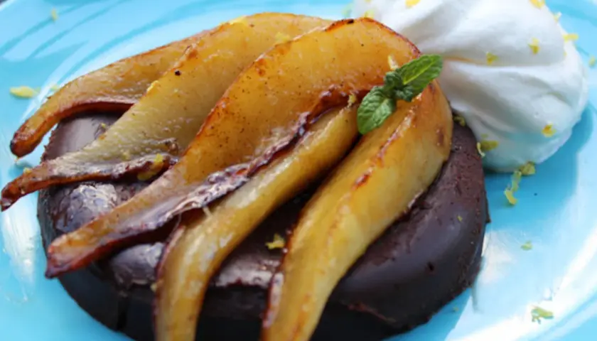 Deliciosa marquesa de chocolate con peras caramelizadas y crema batida, adornada con menta y ralladura de limón.