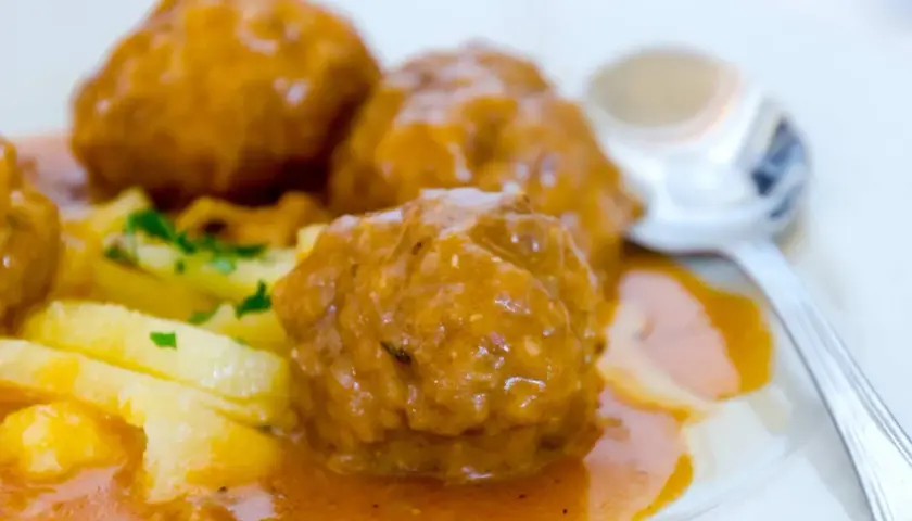 Albondigas a la jardinera, jugosas y cubiertas de salsa, acompañadas de patatas y perejil. Un plato casero listo para disfrutar.