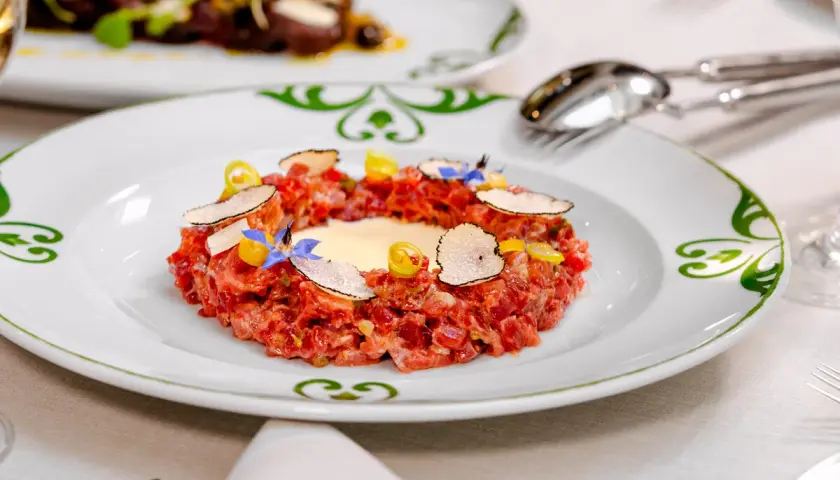 Delicioso tartar de atún fresco, adornado con láminas de trufa negra, flores comestibles y un toque de limón.
