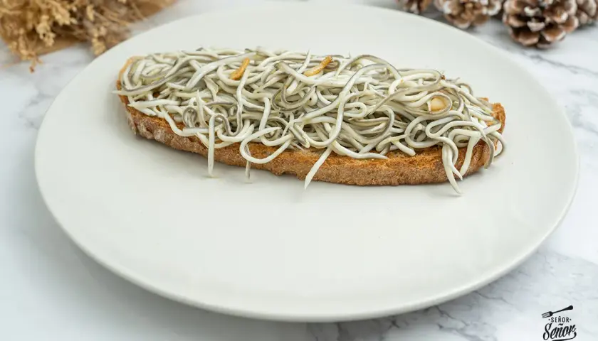 Tosta con gulas al ajillo, un clásico de las recetas con gulas, servida en plato blanco.