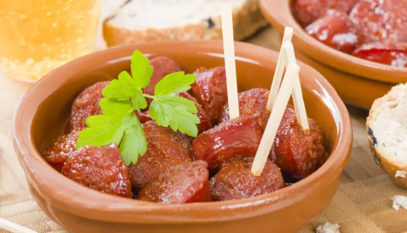 Delicioso chorizo a la sidra en cazuela de barro, adornado con perejil fresco. Acompañado de pan y una cerveza.