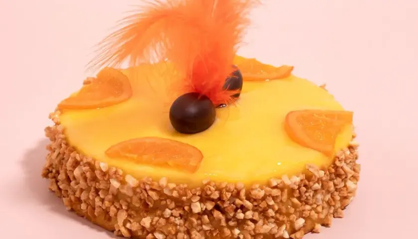 Deliciosa mona de Pascua catalana con glaseado amarillo, rodajas de naranja, chocolate y plumas naranjas.