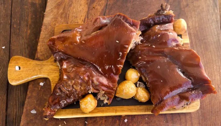 Delicioso cochinillo al horno, receta de la abuela, servido con patatas asadas sobre tabla de madera.