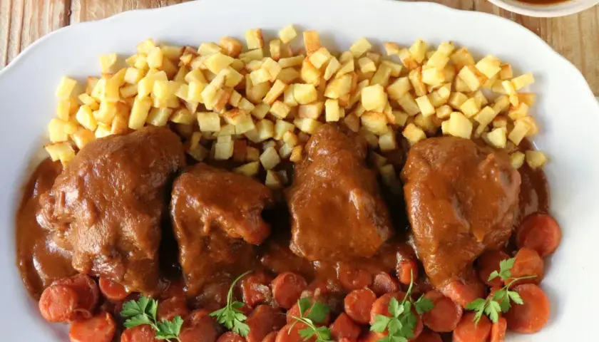 Delicioso jarrete de ternera estofado, acompañado de patatas fritas crujientes y zanahorias en rodajas.