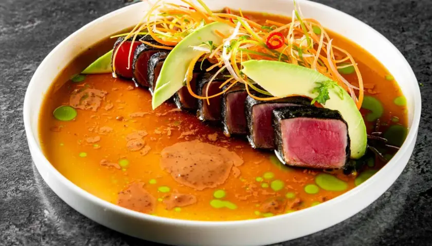 Tataki de atún sellado, servido en un caldo vibrante con aguacate, zanahoria rallada y un toque picante.