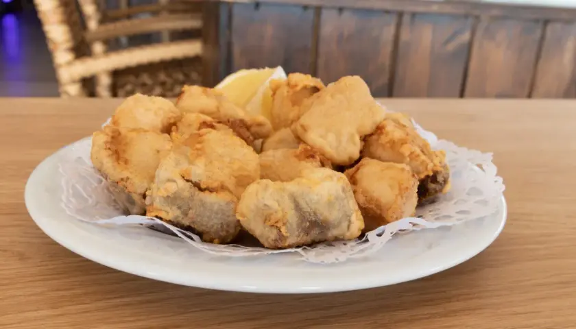 Plato de cazon en adobo, trozos de pescado frito y dorado, servido con una rodaja de limón.