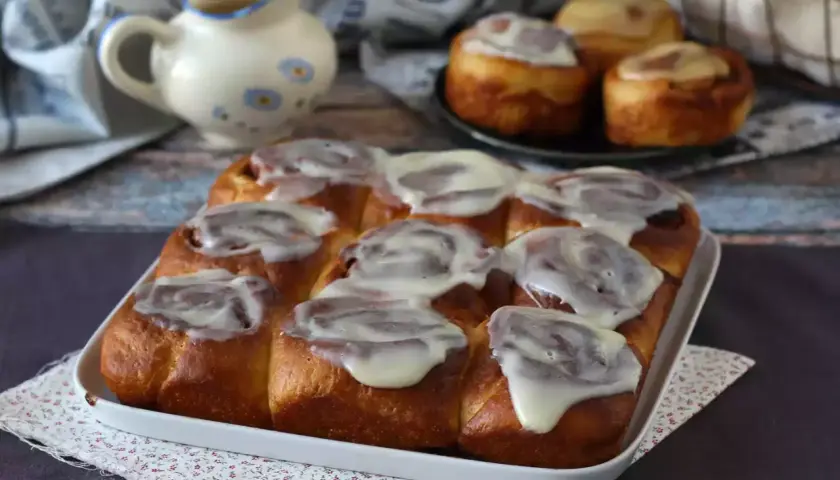 Deliciosos rollitos de canela recién horneados, cubiertos con un glaseado blanco cremoso, listos para ser disfrutados.