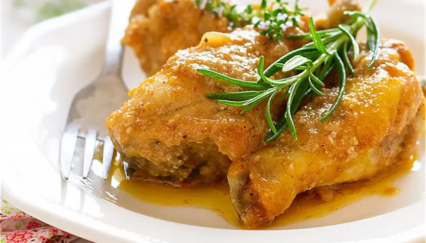 Pollo en salsa de la abuela, jugoso y dorado, servido en plato blanco con romero fresco. Un clásico casero.