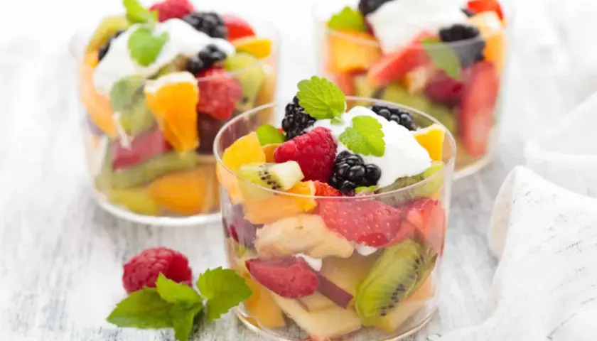 Deliciosa macedonia de frutas con fresas, kiwi, naranja, frambuesas y moras, coronada con crema y menta.