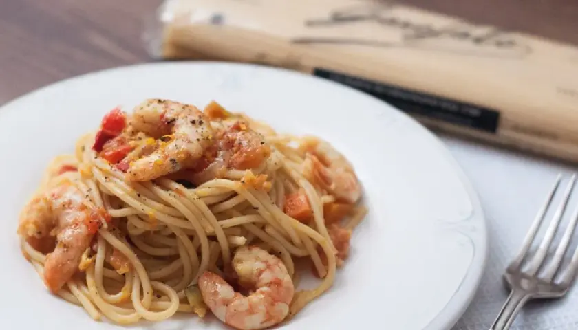 Espaguetis con gambas y trocitos de tomate, servidos en un plato blanco. Un tenedor plateado descansa a la derecha.
