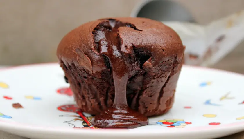 Coulant de chocolate tibio con centro líquido, servido en un plato blanco con dibujos de colores.