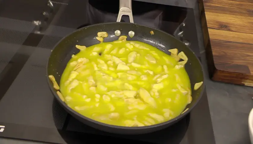 El bacalao al pil pil burbujea en la sartén, con trozos de ajo dorándose en el aceite.