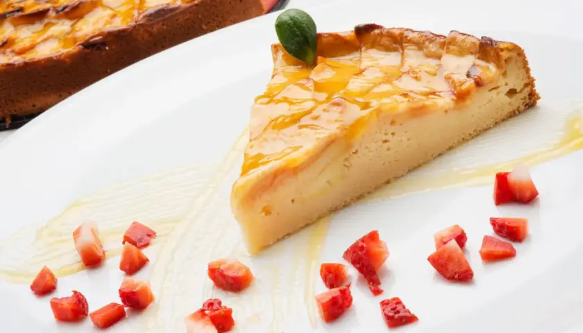 Una rebanada de tarta de manzana tradicional, glaseada y decorada con fresas picadas y una hoja verde.