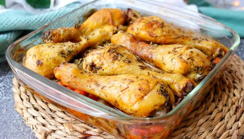 Muslos de pollo al horno dorados y jugosos, sazonados con hierbas aromáticas, servidos en una fuente de vidrio.