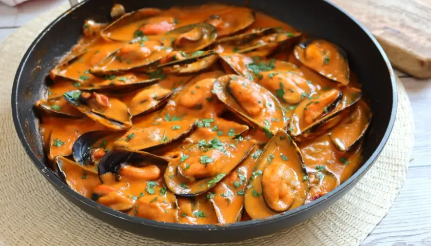 Mejillones con tomate en salsa cremosa, espolvoreados con perejil fresco. Un plato delicioso y fácil de preparar.