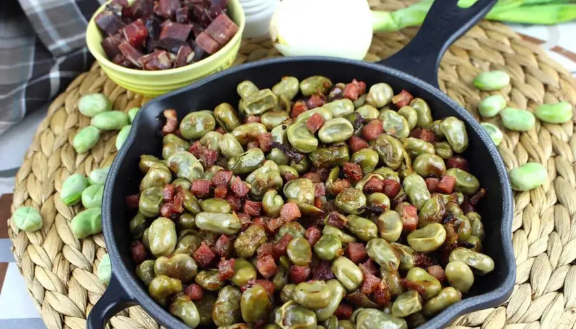 Habas tiernas salteadas con trocitos de jamón en una sartén de hierro fundido, un plato tradicional lleno de sabor.
