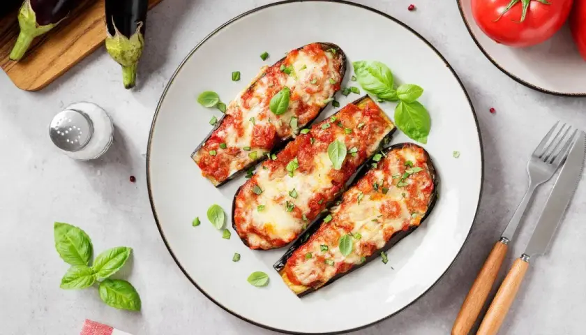 Berenjenas asadas con tomate y queso, un plato delicioso de recetas con berenjenas. Decoradas con albahaca fresca.