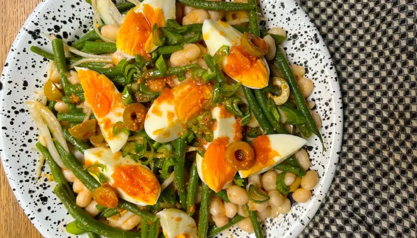 Ensalada de judías verdes, huevos duros, alubias blancas y aceitunas, aderezada con cebolleta picada.