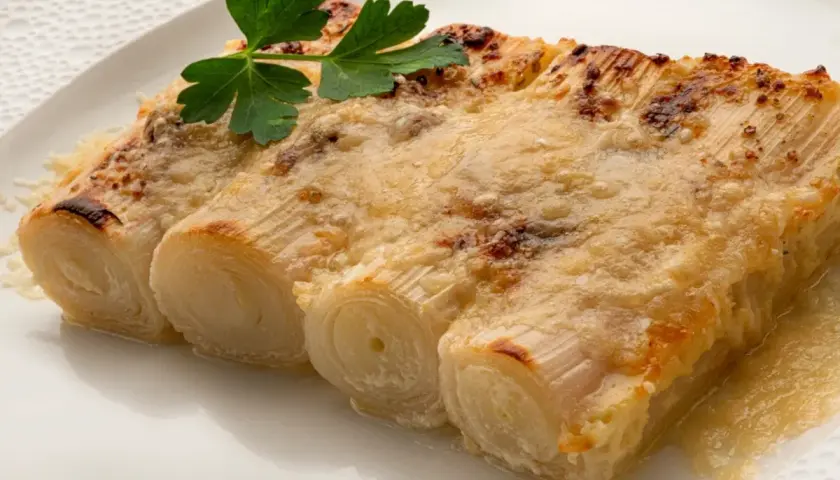 Tres tiernos puerros al horno gratinados con queso, coronados con una ramita de perejil fresco.