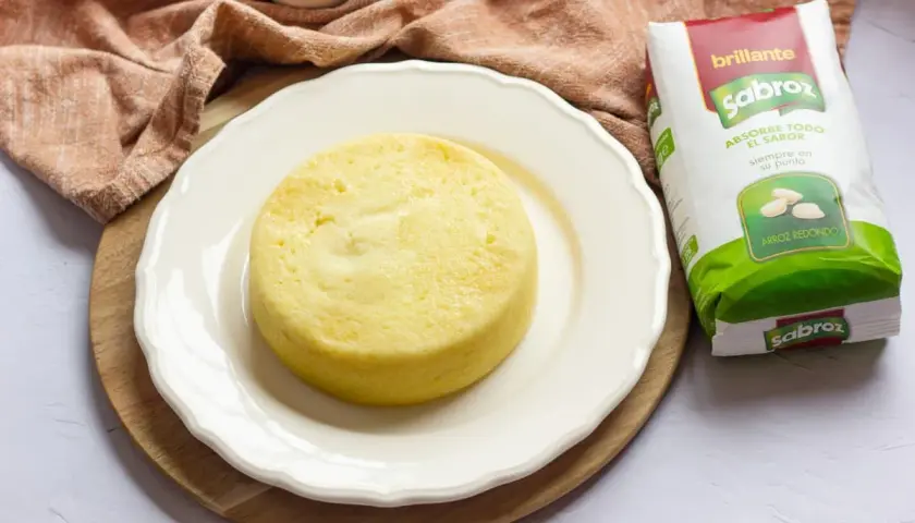Pastel de arroz dorado y esponjoso en plato blanco, junto a un paquete de arroz Sabroz.