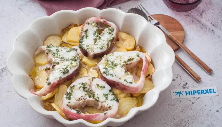 Rodajas de pescado rosado al horno con patatas, cubiertas de hierbas frescas.