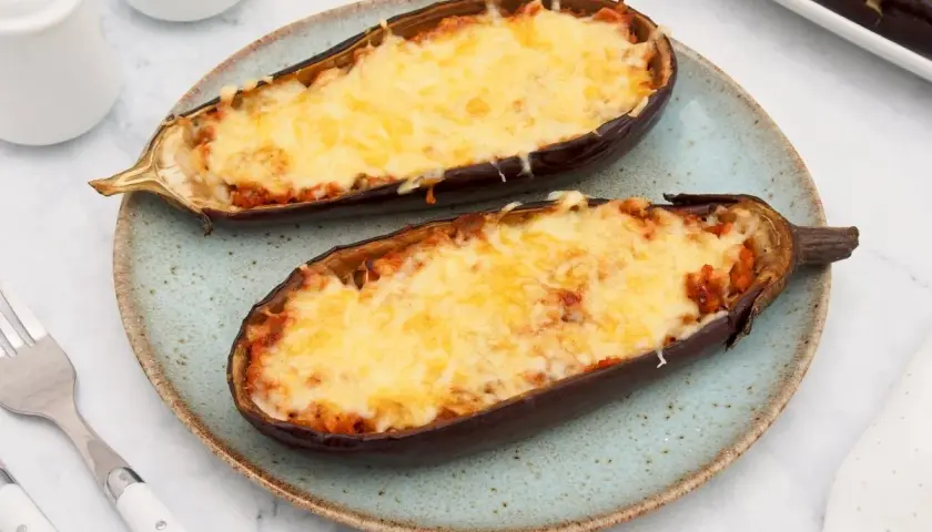 Dos mitades de berenjenas rellenas de atún, gratinadas con queso derretido, servidas en un plato azul.