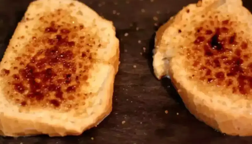 Dos rebanadas de pan tostado con azúcar caramelizada encima, listas para ser horneadas como torrijas.