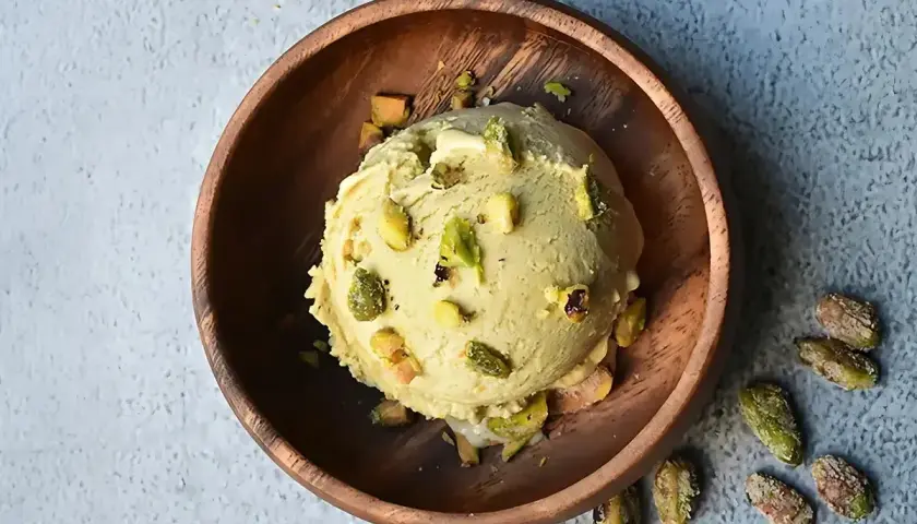 Cremoso helado de pistacho, adornado con trozos de pistacho, servido en un cuenco de madera rústico.