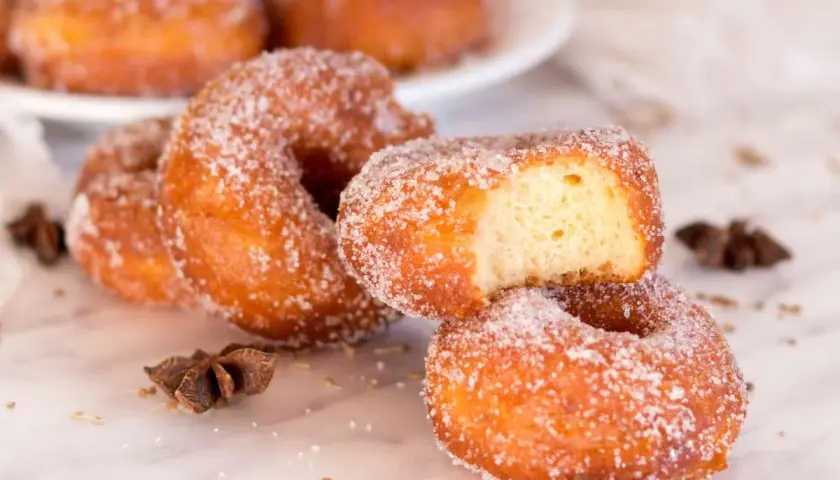 Rosquillas de carnaval espolvoreadas con azúcar, una con un mordisco, junto a anís estrellado.
