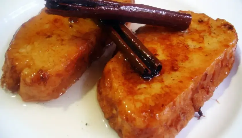 Dos deliciosas torrijas de vino, doradas y bañadas en almíbar, coronadas con canela en rama.