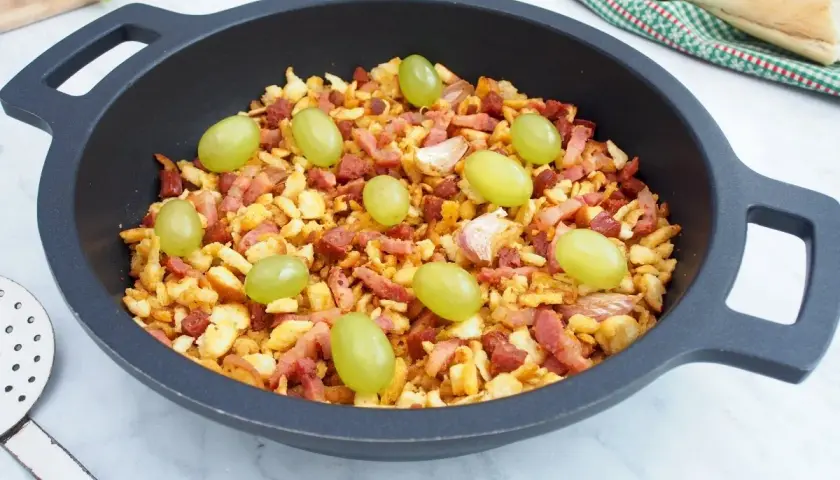 Migas manchegas con uvas verdes y ajos en una sartén. Un plato tradicional listo para disfrutar.