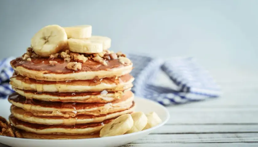 Una pila de tortitas de plátano cubiertas de miel y nueces, con rodajas de plátano fresco encima.