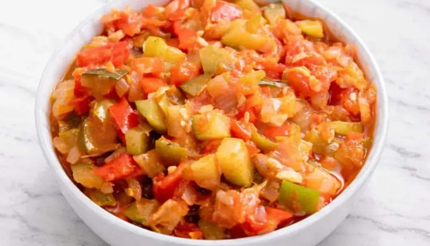 Un tazón blanco lleno de pisto manchego, un guiso vibrante de verduras picadas como tomate, pimiento y calabacín.